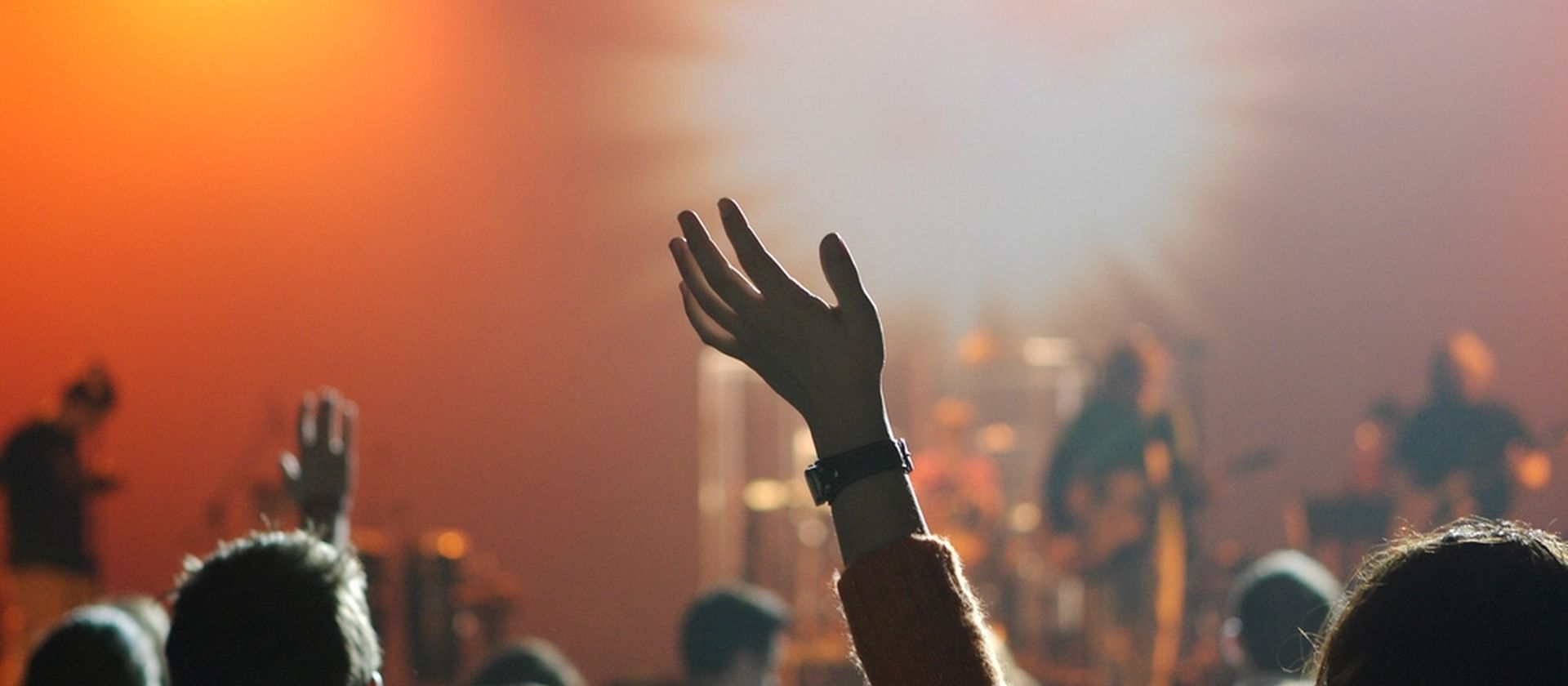 Hands lifted in worship as warm light breaks over a gathered congregation
